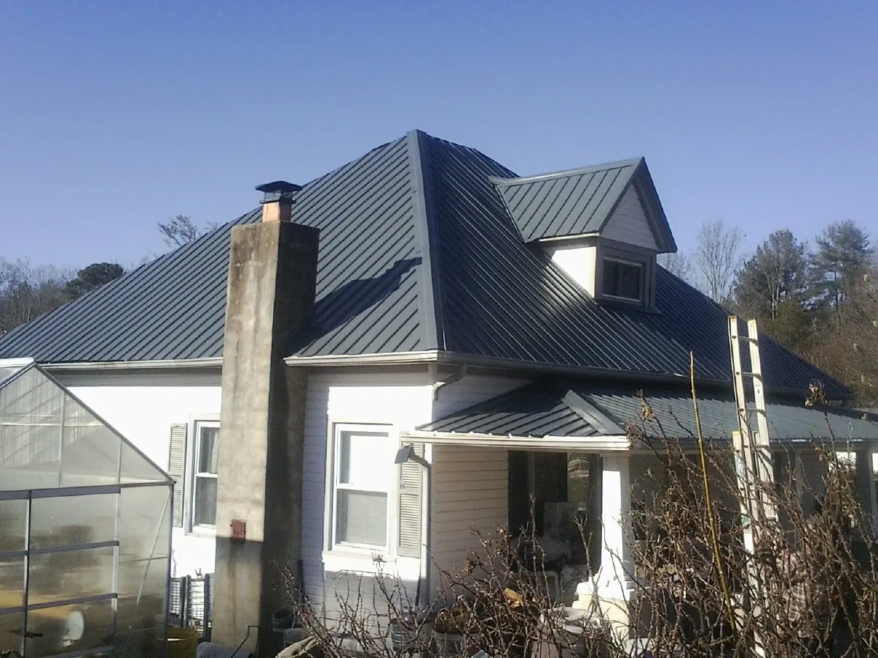Dark blue standing seam metal roof on a white farmhouse with dormer — Slate & Tile Roof Repair by Roofing Brothers in Quenemo