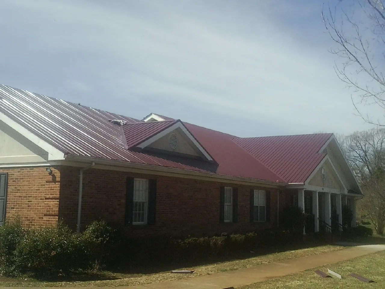 Red metal roof with gabled entries on a long brick building, from a Hail Damage Roof Repair job in Quenemo