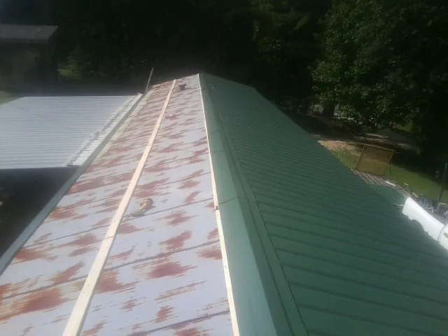 Old rusted panels beside newly installed green metal roofing — Wind Damage Roof Repair by Roofing Brothers in Quenemo