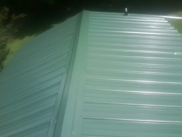 New green metal panels meeting at the ridge of a roof — Flat Roof Repair work by our crew in Quenemo