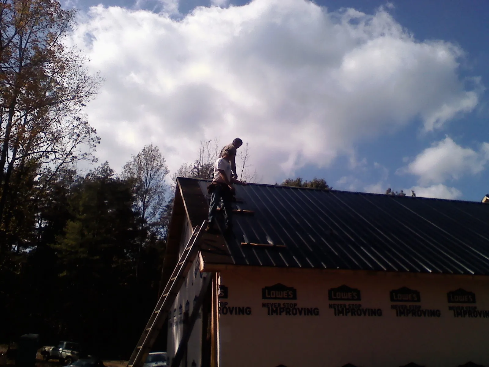 Roofer fastening dark metal panels high against a cloudy sky, from a Roof Inspection job in Quenemo