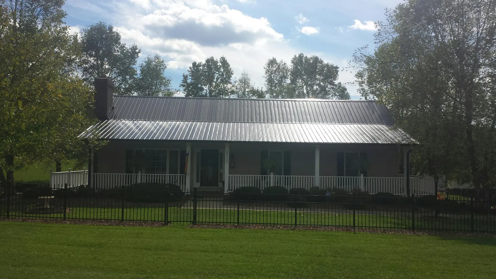 Gray metal roof on a brick ranch with a full width front porch — Gutter Guard Installation work by our crew in Quenemo
